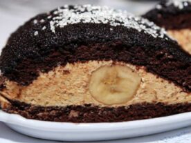Szeletelt 'Elefánt könnycsepp' sütemény sötét piskótából, világos diós-vaníliás krémmel töltve, középre helyezett banánszelettel, porcukorral meghintve a tetején.