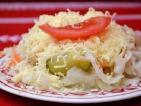 Bolgár saláta: Tányéron tálalt, reszelt sajttal megszórt vegyes saláta, középen zöldpaprika szelettel és tetején paradicsom cikkel díszítve.