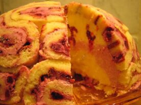 Gömbölyű, rétegezett Bomba-jó torta piskótatekercs szeletekkel és gyümölcsös töltelékkel, amely részben felszeletelve mutatja meg belsejét.
