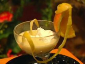 Egy elegáns üvegpohárban tálalt Borleves mazsolával, tejszínhabbal a tetején és dekoratív citrushéj-spirállal díszítve, amely az édesség oldalára van helyezve.