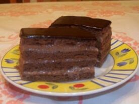 Egy szelet házi készítésű Sport szelet egy mintás tányéron, több rétegű kakaós tésztával és sötét csokoládékrémmel, a tetején fényes csokoládémázzal.