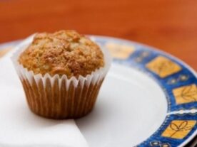 Céklás-körtés muffin: Egy aranybarna tetejű muffin papírkosárkában, tálalva egy kék és sárga mintás kerámiatányéron.