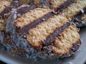 Albert kekszes süti szeletek egy tányéron, csokoládécsíkokkal és kókuszreszelékkel díszítve, a süti rétegei és ropogós szélei jól kivehetőek.