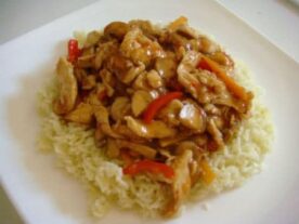 Szecsuáni csirke: Csíkokra vágott csirke és zöldségek gazdag szószban, tálalva fehér rizzsel egy világos tányéron.