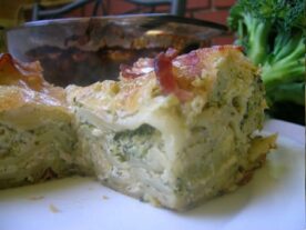 Szelet brokkolis lasagne egy tányéron, a hátterében több lasagne és friss brokkoli.