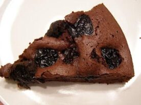 Aszaltszilvás csokitorta: egy szelet csokoládétorta látható egy fehér tányéron, amelynek közepébe nagyobb, egész aszalt szilvák vannak ágyazva, kiemelkedő kontrasztot képezve a sötét csokoládés tésztával.