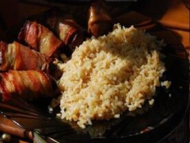 Baconbe tekert csirkemáj és mellékelve fűszeres rizzsel tálalva egy sötét tányéron.
