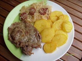 Egy tányéron szervírozott magyar étel, Bagolyvári sertésflekken, mellette párolt savanyú káposztával és aranyszínűre sült burgonyaszeletekkel.