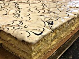 Réteges Bácskai krémes sütemény fehér habbal és csokoládémintával a tetején, tálalásra kész állapotban.