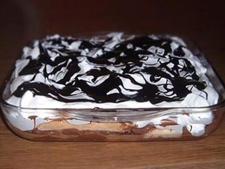 Egy réteges, jénai tálban tálalt Boszorkány máglya desszert, melynek alsó részén babapiskóták, középen gesztenye massza, tetején pedig tejszínhab és csíkokban elosztott csokoládéöntet látható.