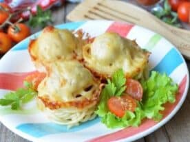Spagetti snack muffinok sajttal megszórva egy tányéron, mellettük friss zöldsaláta levelek és paradicsomszeletek.